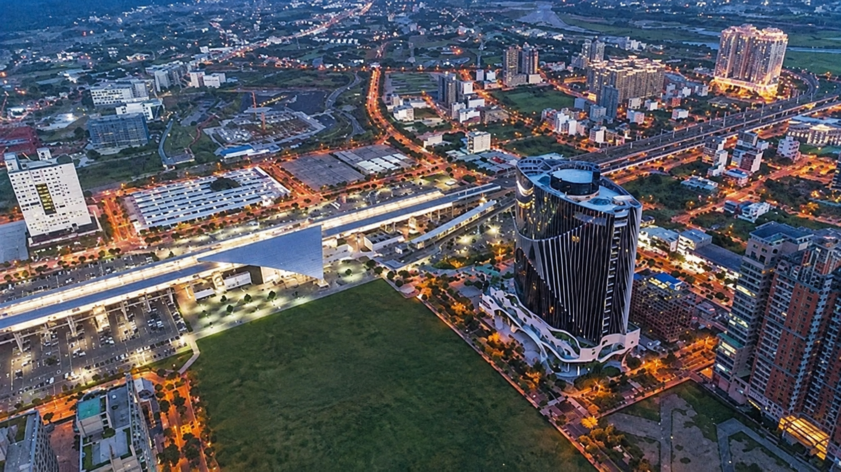 Twilight Cityscape With Green Field And Modern Tower